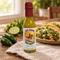 Green Hot Sauce bottle on rustic wood with tacos, lime, and jalapeños